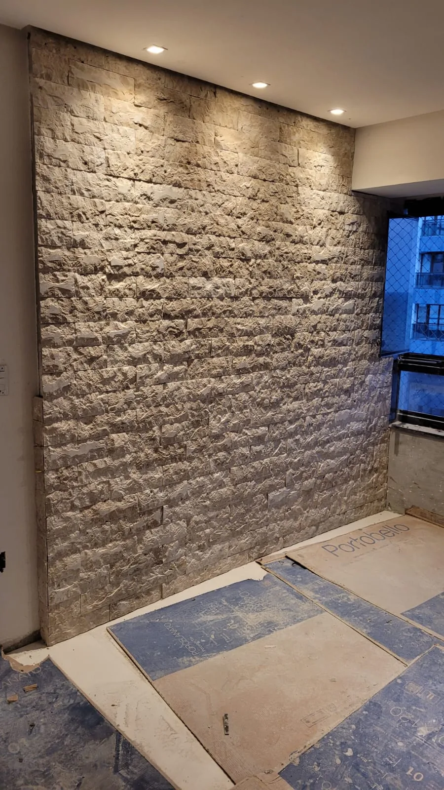 Parede com revestimento de relevo marcado e piso protegido durante a obra.